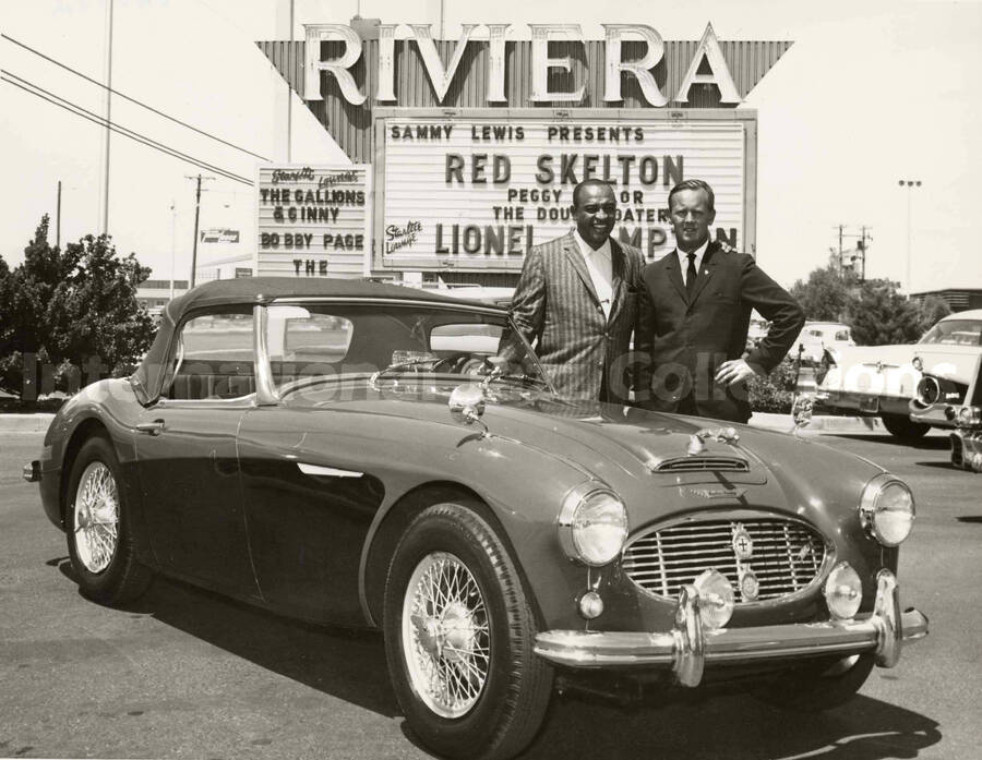 7 x 9 inch photograph. Lionel Hampton poses with unidentified man by a new car, in front of the Riviera [Casino]. An outdoor poster reads: Sammy Lewis presents Red Skelton; Peggy Taylor; The Double Daters; Lionel Hampton