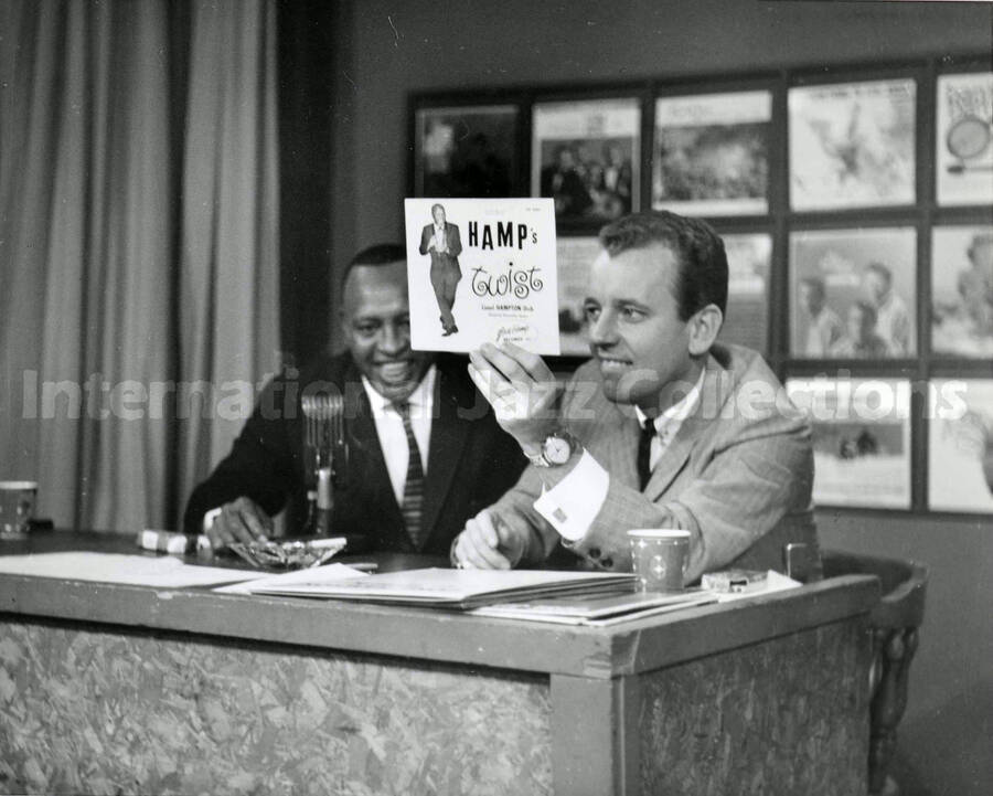 8 x 10 inch photograph. Lionel Hampton with unidentified man [in a radio studio?]. The man is holding a copy of the record Hamp's Twist (Glad-Hamp Records)