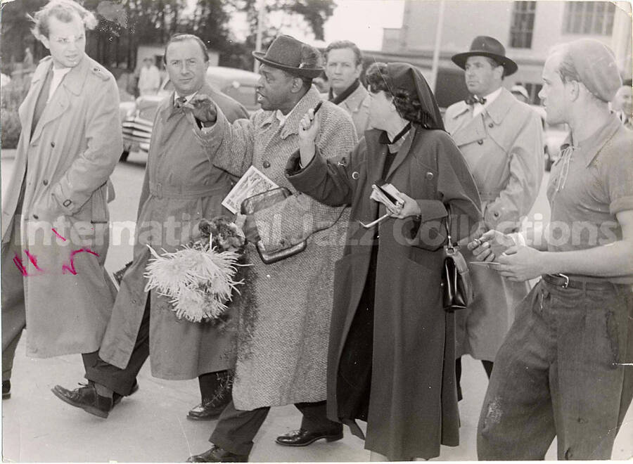 5 3/4 x 7 3/4 inch photograph. Lionel Hampton with unidentified persons, walking outside an airport [in Germany?]
