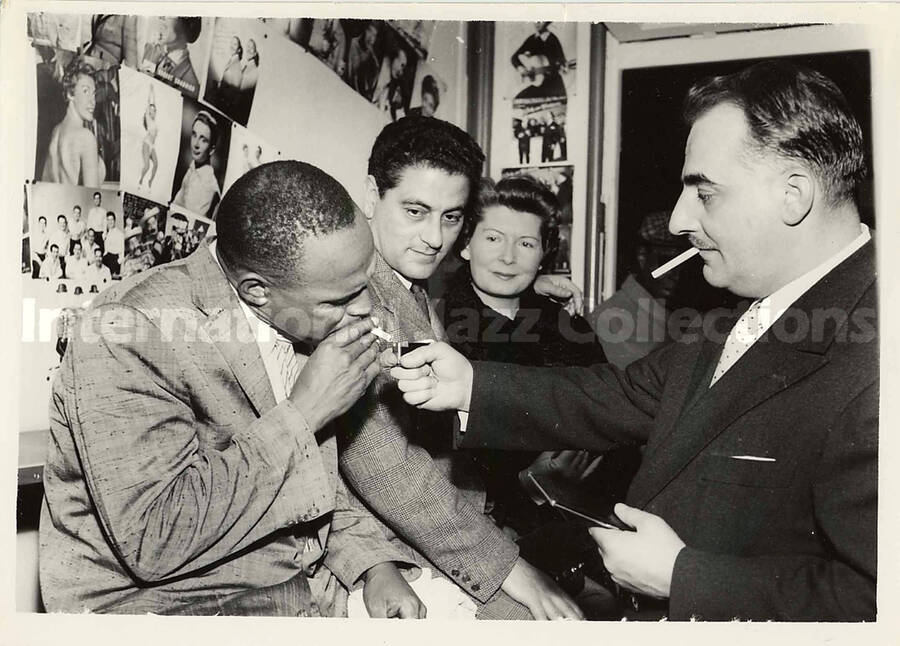 5 x 7 inch photograph. Lionel Hampton with unidentified persons [abroad?]. Hanging on a wall pictures of several artists