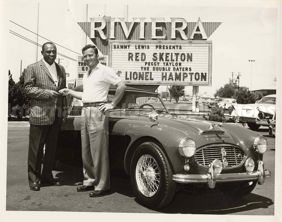 7 x 9 inch photograph. Lionel Hampton poses with unidentified man by a new car, in front of the Riviera [Casino]. An outdoor sign reads: Sammy Lewis presents Red Skelton; Peggy Taylor; The Double Daters; Lionel Hampton