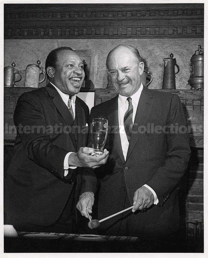 10 x 8 inch photograph. Lionel Hampton with unidentified man. On the shelf behind them appears a collection of [German?] beer steins