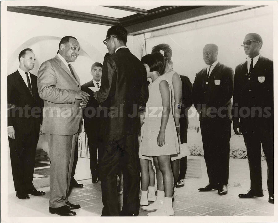 8 x 10 inch photograph. Lionel Hampton at a formal reception. Handwritten on the back of the photograph: King of the vibes meets king of Thailand