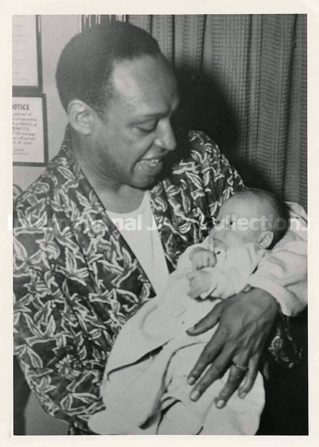 7 x 5 inch photograph. Lionel Hampton holding a baby. Handwritten on the back of the photograph: Joan (Markee) Manino
