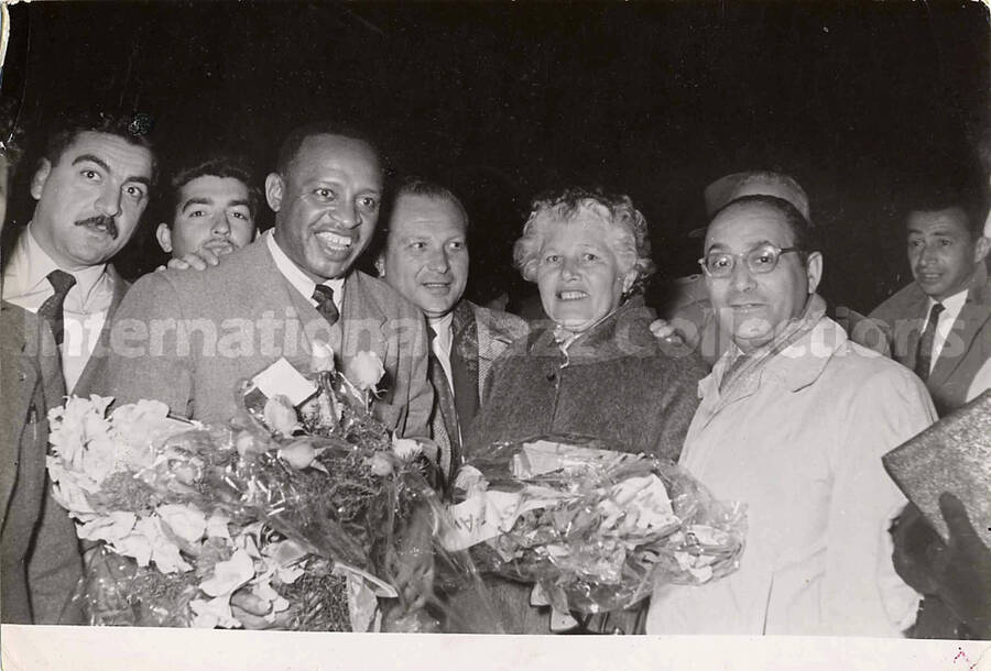 5 x 7 inch photograph. Lionel Hampton with unidentified persons in Israel. Handwritten on the back of the photograph: Lydda Airport, meeting by officials