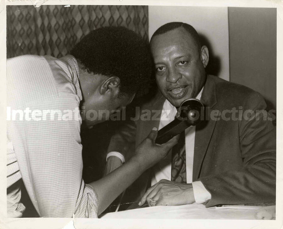8 x 10 inch photograph. Lionel Hampton speaking on a microphone hold by unidentified man, probably during his tour in Africa