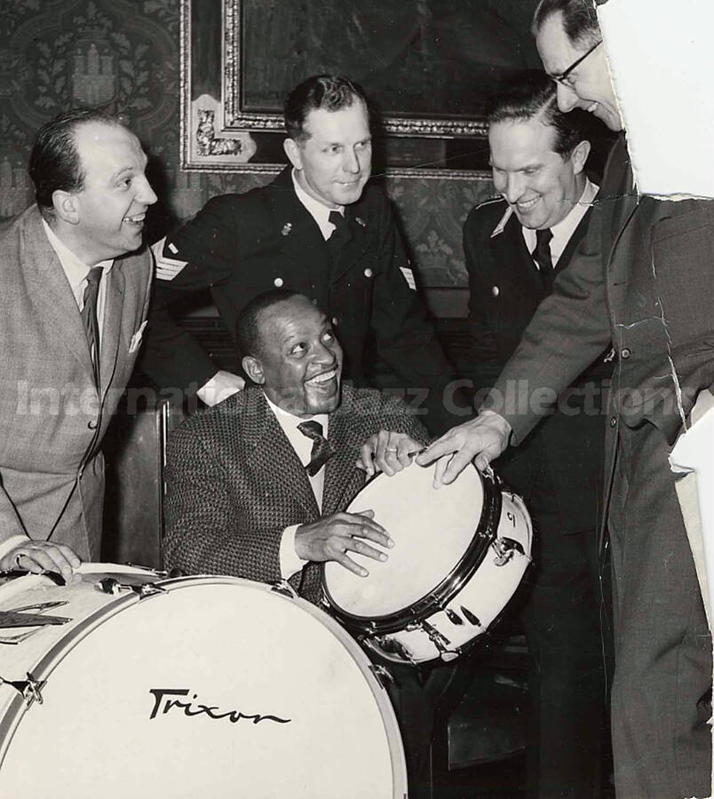 5 3/4 x 5 inch photograph. Lionel Hampton by a set of Trixon drums with unidentified men, including two military figures [in Hamburg, Germany]. On the back of the photograph is a typewritten note in German
