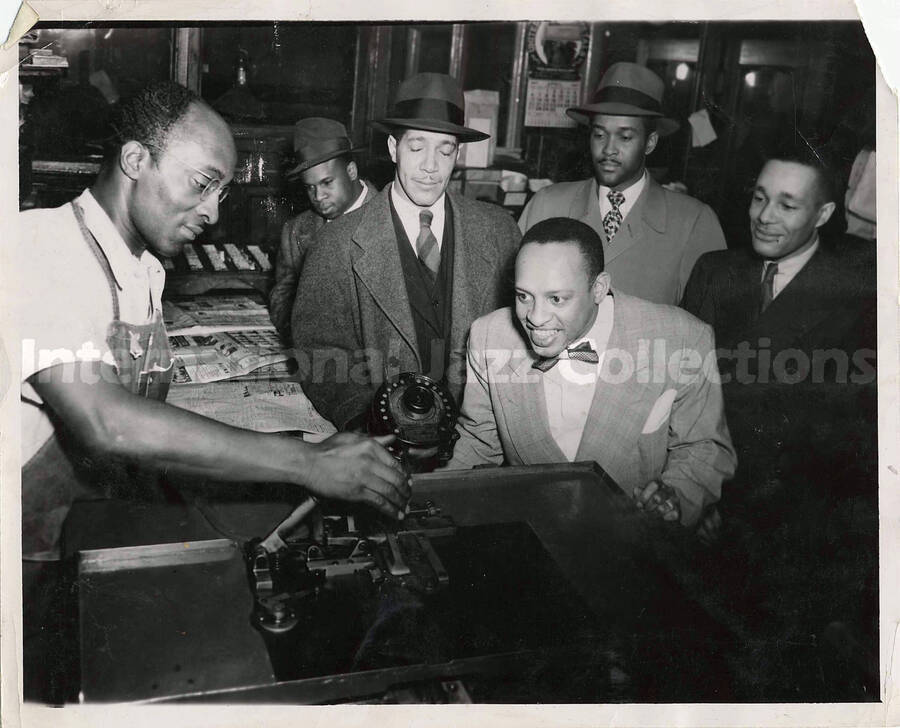 8 x 10 inch photograph. Lionel Hampton with unidentified men [at a newspaper press?]. Handwritten on the back of the photograph: Lionel Hampton and Ludlow