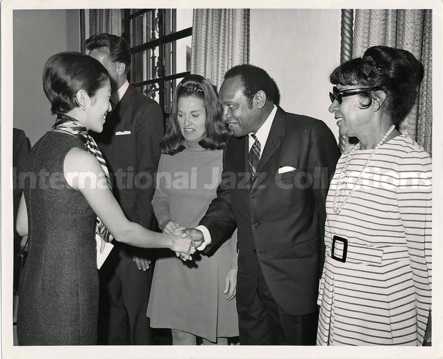 8 x 10 inch photograph. Gladys and Lionel Hampton at a formal reception. Handwritten on the back of the photograph: Lionel Hampton shakes hands with Japanese Princess Suganomiya[?] at a reception held in the residence of the US Ambassador to Japan, Tokyo