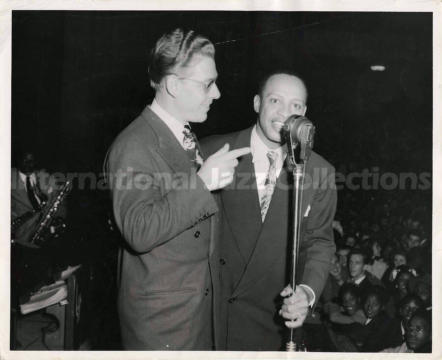 8 x 10 inch photograph. Lionel Hampton at the microphone with unidentified man on a stage in front of an audience