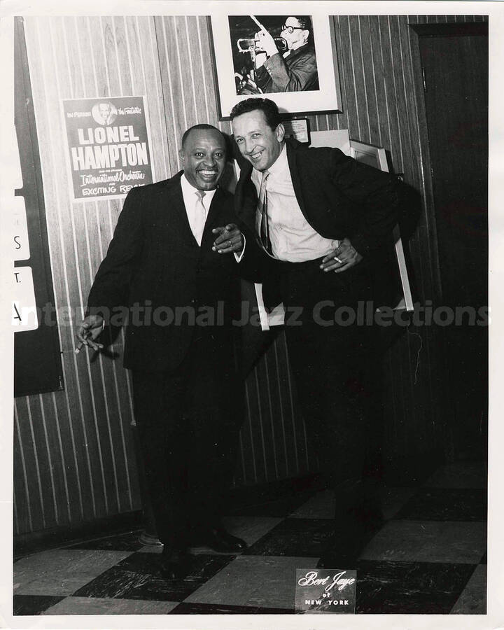 10 x 8 inch photograph. Lionel Hampton with unidentified man in front of a poster of the Le Jazz Hot. The poster, written in French, announces his performance on Sep. 21