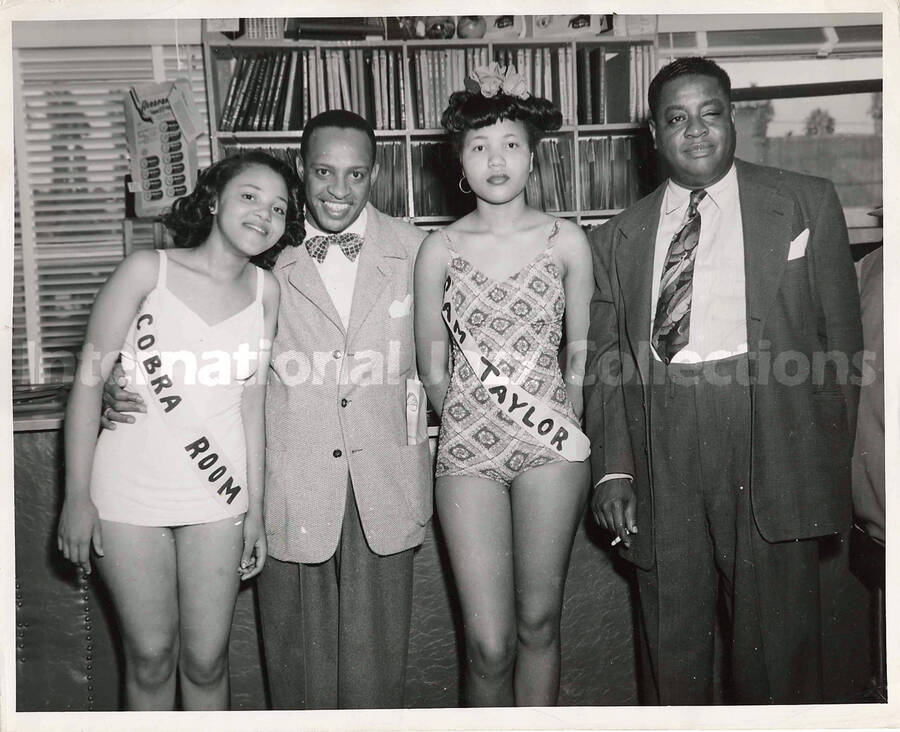 8 x 10 inch photograph. Lionel Hampton with a group of unidentified persons including two women wearing sashes. The sashes of women reads: Cobra Room and Sam Taylor