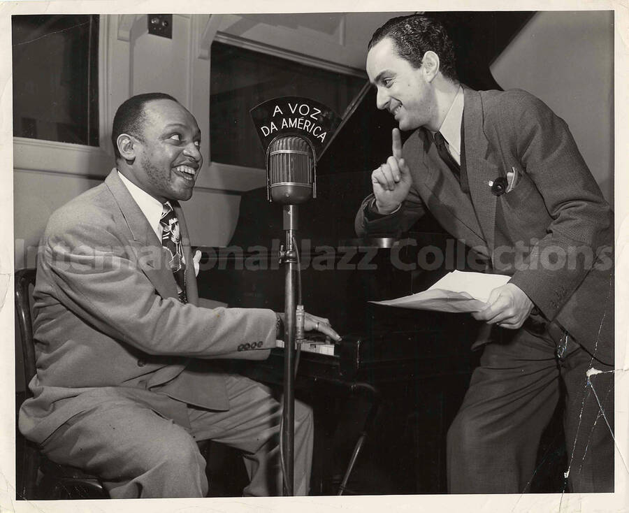 8 x 10 inch photograph. Lionel Hampton with unidentified man, probably at Voice of America Headquarters in Washington, DC, broadcasting programming aimed at Brazil