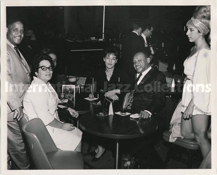 8 x 10 inch photograph. Lionel Hampton with unidentified persons in a club. Cards on the tables read: Al Hirt; Champagne Luncheon