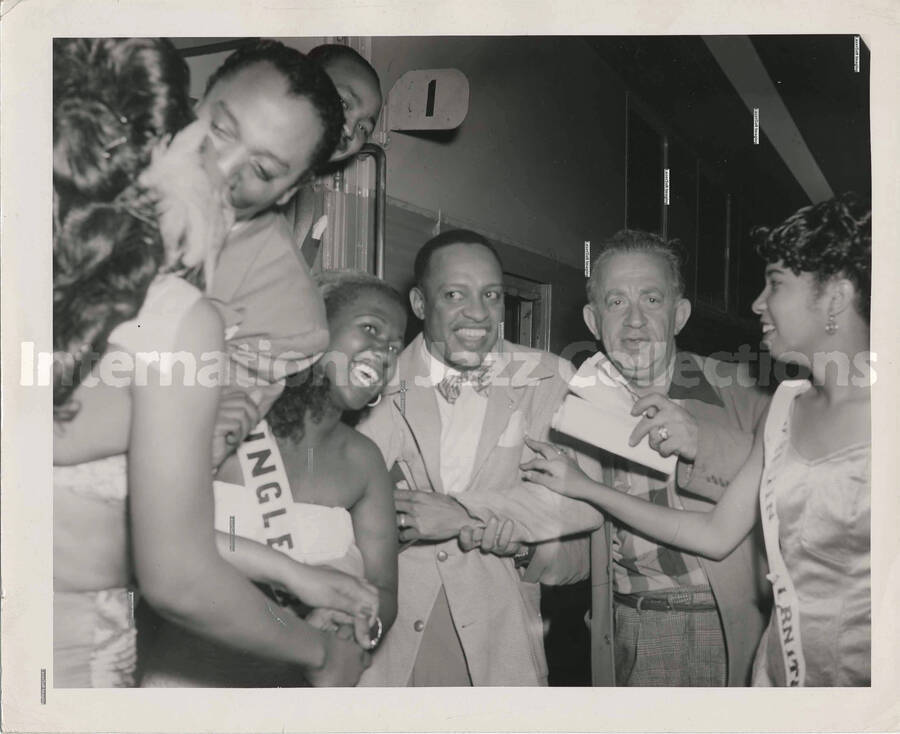 8 x 10 inch photograph. Lionel Hampton with a group of unidentified persons, boarding a train including Miss Sam Taylor