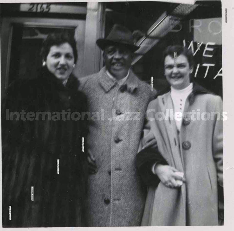 3 1/2 x 3 1/2 inch photograph. Lionel Hampton with two women, [in Canada]. Handritten on the back of the photograph: Josi Bonomo (left), (Montreal); Joan Miller (right), (Montreal)