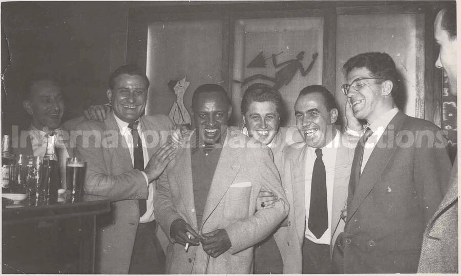 3 1/2 x 5 1/2 inch photograph in the format of postcard. Lionel Hampton with unidentified men. Handwritten on the back of the photograph: Just a little memory from the band of Frascati's Stuttgart-Germany