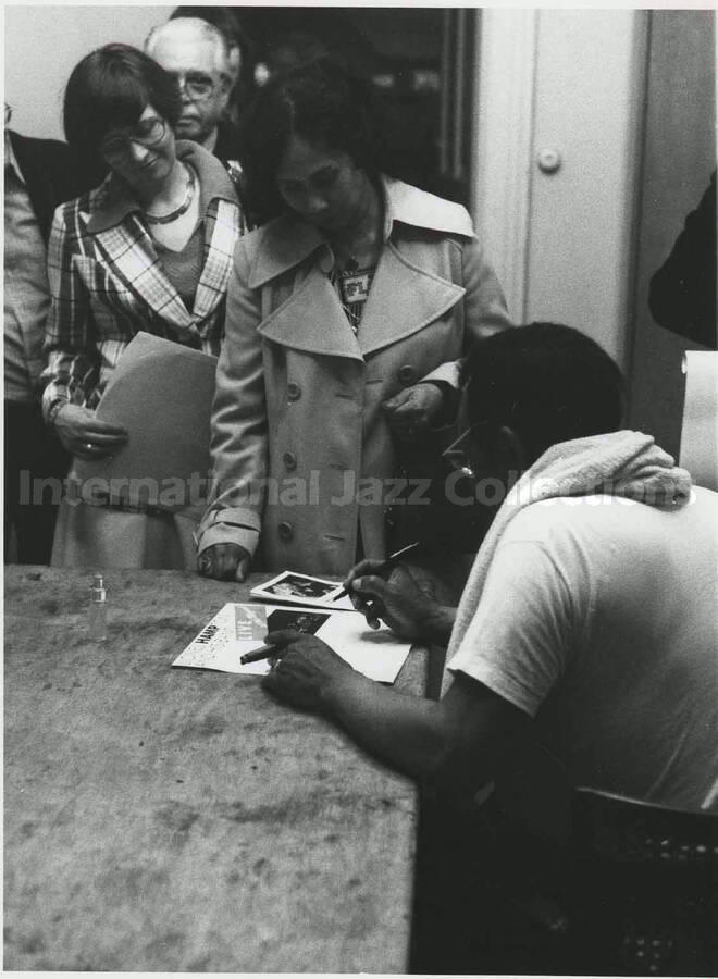 5 1/2 x 4 inch photograph. Lionel Hampton signs a copy of his record Lionel Hampton and His Band Live at Muzeval