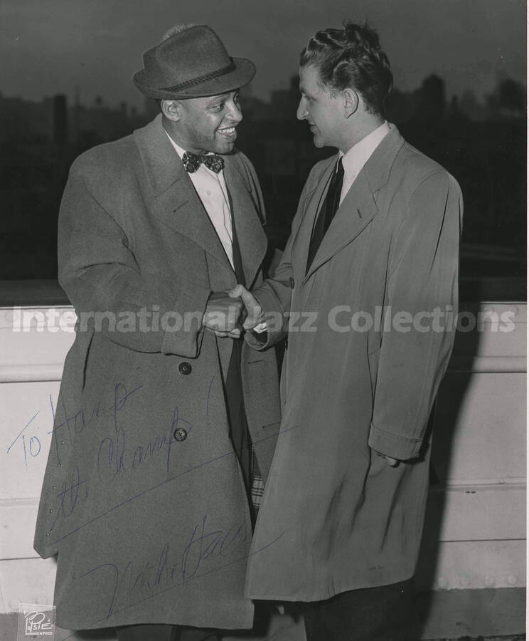 10 x 8 inch photograph. Lionel Hampton on board of a ship shaking hands with unidentified man. This photograph was probably taken  on his return to the United States after a tour in Europe. It is dedicated to Lionel Hampton from Mike Hall [?]