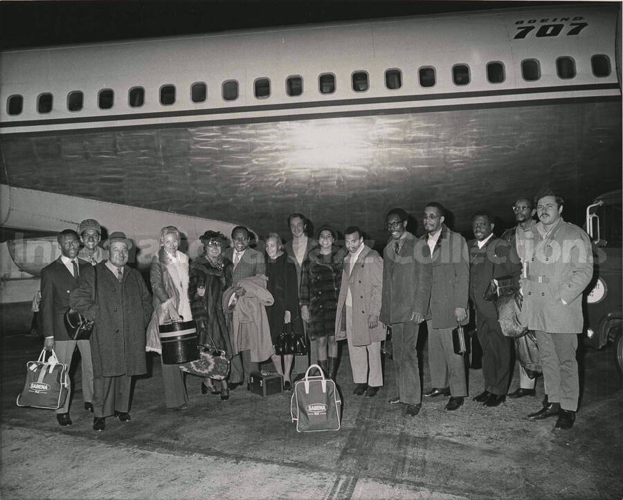 8 x 10 inch photograph. Lionel and Gladys Hampton with band standing outside a Boeing 707. Present are guitarist Billy Mackel, Bill Titone, and others