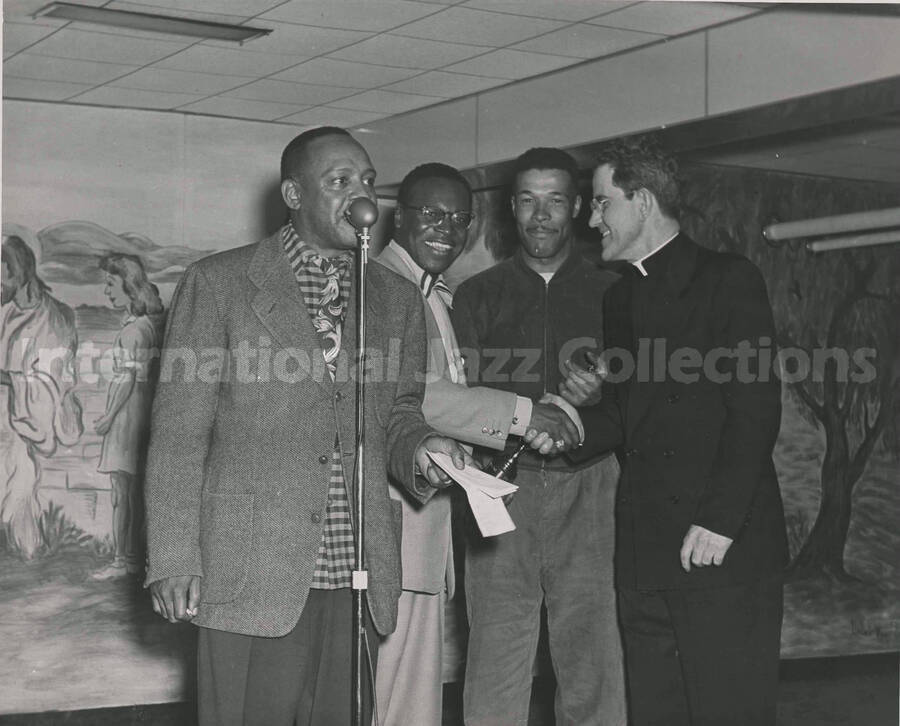8 x 10 inch photograph. Lionel Hampton with three unidentified men, including a priest. One of the men is holding a trophy