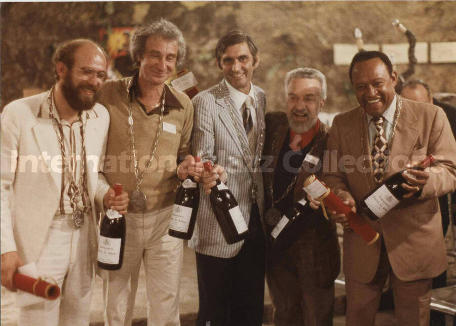 5 x 7 inch photograph. Lionel Hampton, Bill Titone, and three unidentified men holding bottles of wine, in France. They are wearing medals of the Commanderie des Costes du Rh?ne