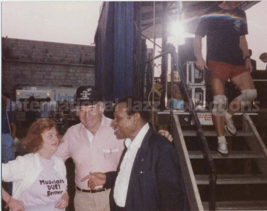 3 1/2 x 4 1/2 inch photograph. Lionel Hampton back stage with George Wein and unidentified woman. Wein is wearing a hat of the 1985 Newport Folk Festival