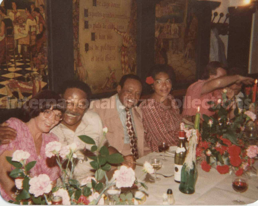 3 1/2 x 4 1/2 inch photograph. Lionel Hampton with unidentified persons in a restaurant. Handwritten on the back of the photograph: Le Merle Blanc, Nice, France