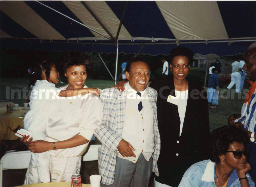 3 1/2 x 5 inch photograph. Lionel Hampton with unidentified persons under a tent, on the occasion of the Jazzy [Summer jazz festival in Yonkers, NY?]