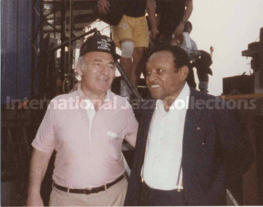 3 1/2 x 4 1/2 inch photograph. Lionel Hampton back stage with George Wein. Wein is wearing a hat of the 1985 Newport Folk Festival