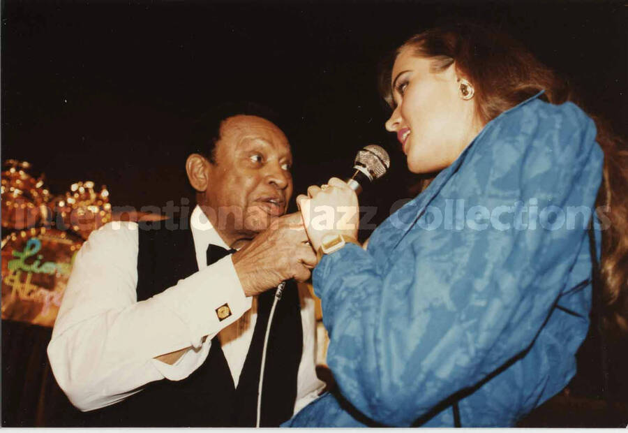 3 1/2 x 5 inch photograph. Lionel Hampton holds microphone for an unidentified woman to speak