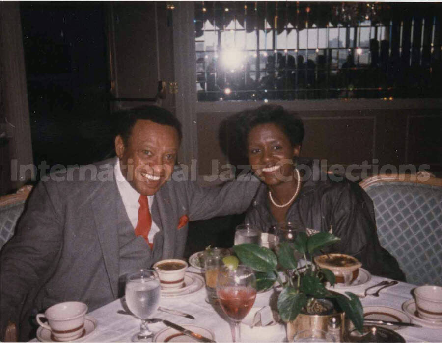 3 1/2 x 4 1/2 inch photograph. Lionel Hampton sits at a dinner table with unidentified woman