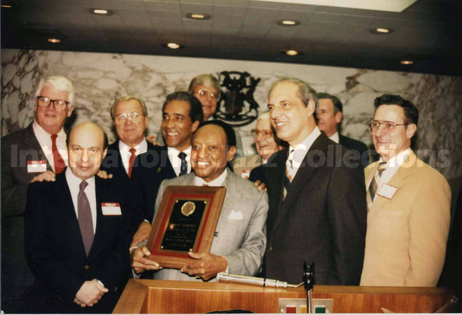 3 1/2 x 5 inch photograph. Lionel Hampton holds a plaque surrounded by unidentified persons, in Detroit, Michigan
