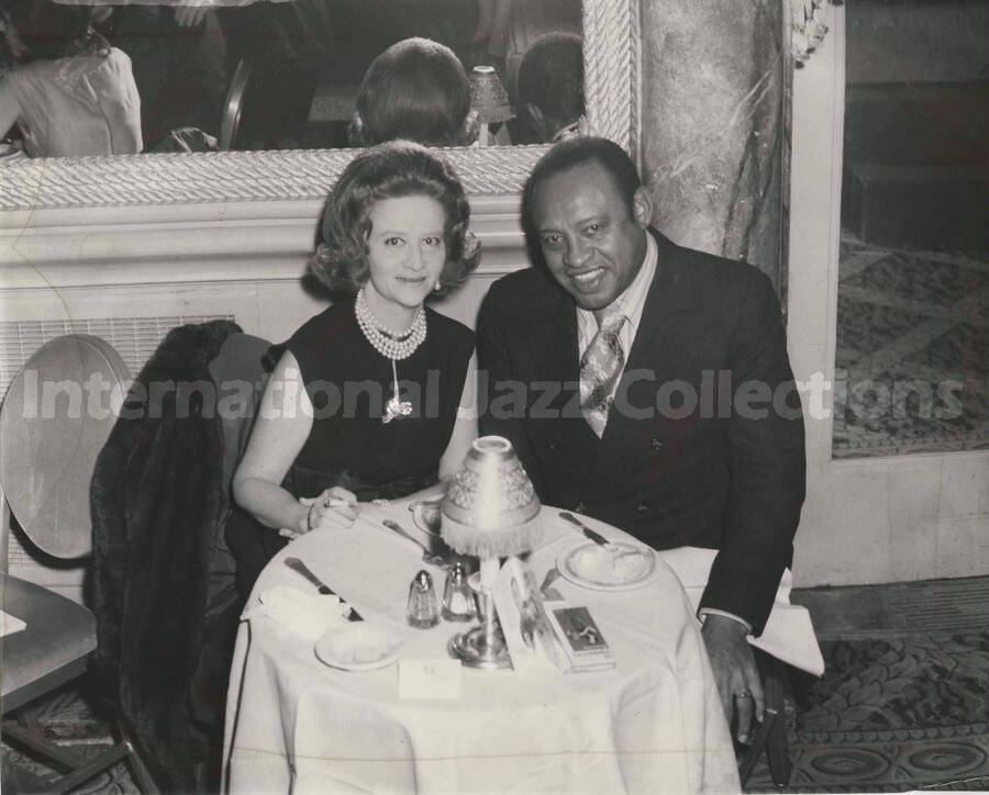 8 x 10 inch photograph. Lionel Hampton with unidentified woman in a restaurant. Accompanying this photograph is a portfolio from the Empire Room of The Waldorf Astoria Hotel, in New York, NY