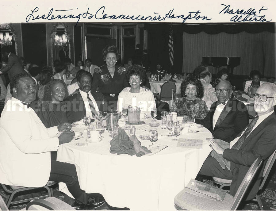 8 x 10 inch photograph. Unidentified persons in a restaurant. Handwritten on the photograph: Listening to Commissioner Hampton; Marcella & Alberta