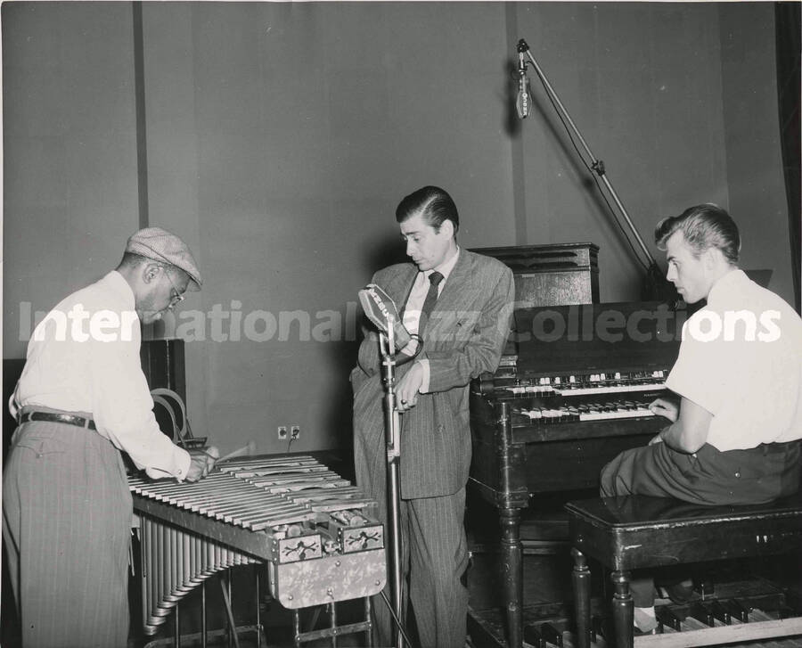 8 x 10 inch photograph. Lionel Hampton playing the vibraphone observed by an unidentified man and Doug Duke at the piano, at the KNBC studio