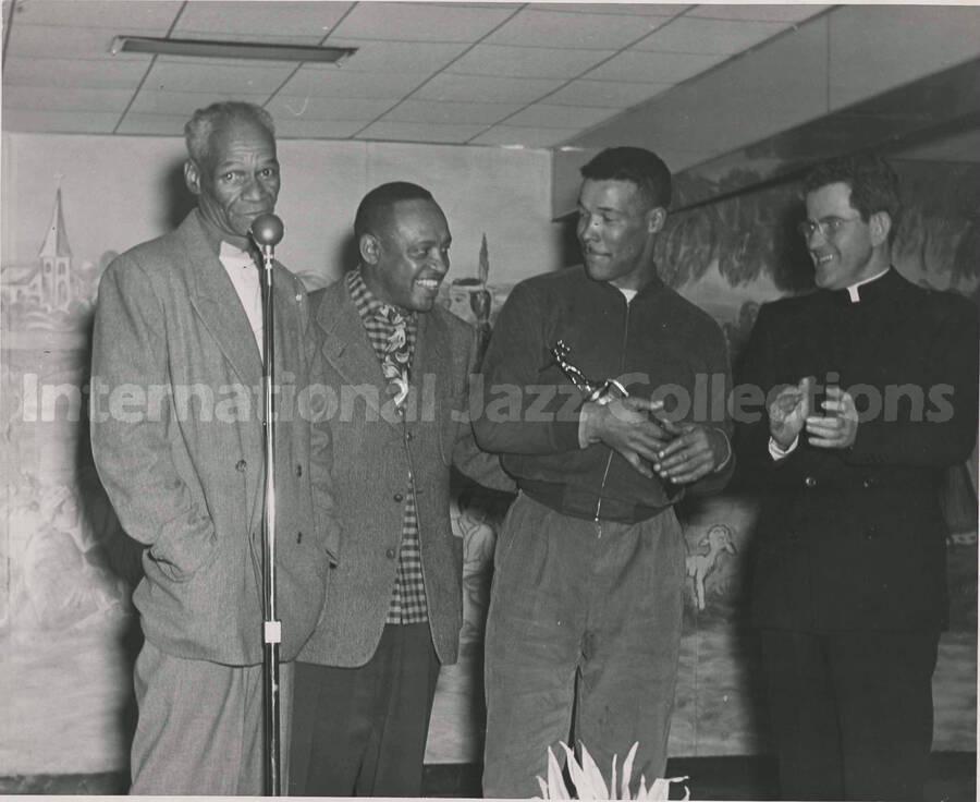 8 x 10 inch photograph. Lionel Hampton with three unidentified men, includin a religious. One of the men is holding a trophy