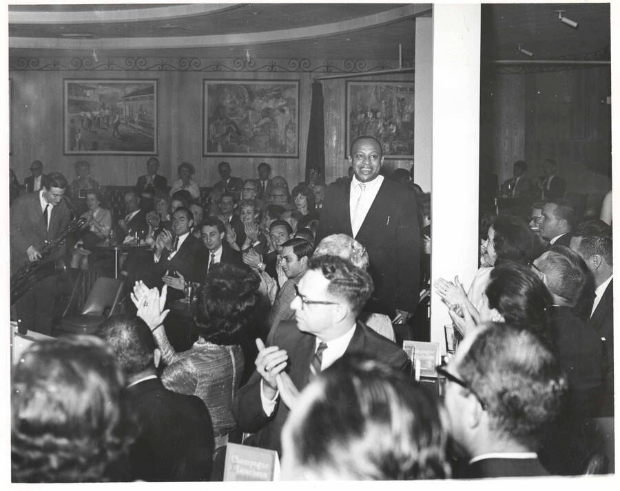 8 x 10 inch photograph. Lionel Hampton with unidentified persons at a club. Cards on the tables read: Champagne Luncheon