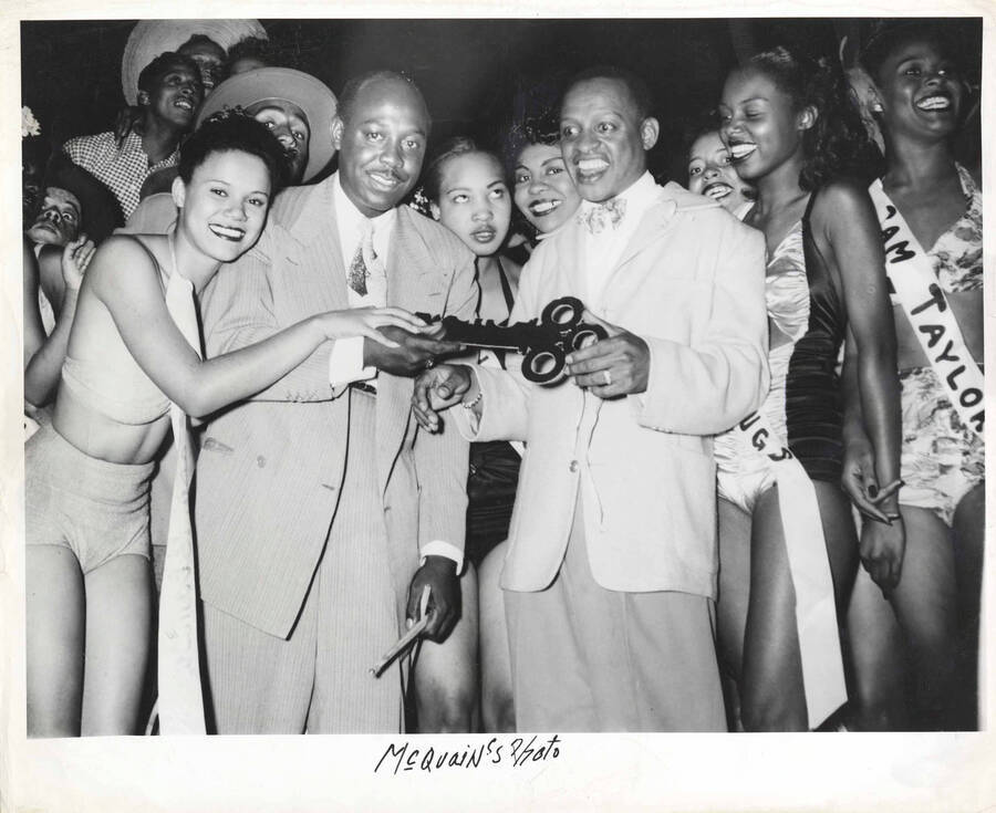 8 x 10 inch photograph. Lionel Hampton and Roy Milton holding a ceremonial key with unidentified women wearing sashes; one reads: Sam Taylor
