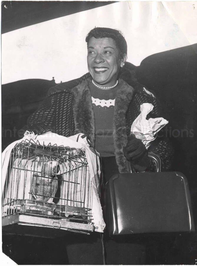 9 1/2 x 7 inch photograph. Gladys Hampton carrying a cage with a parrot in it [in Paris, France?]