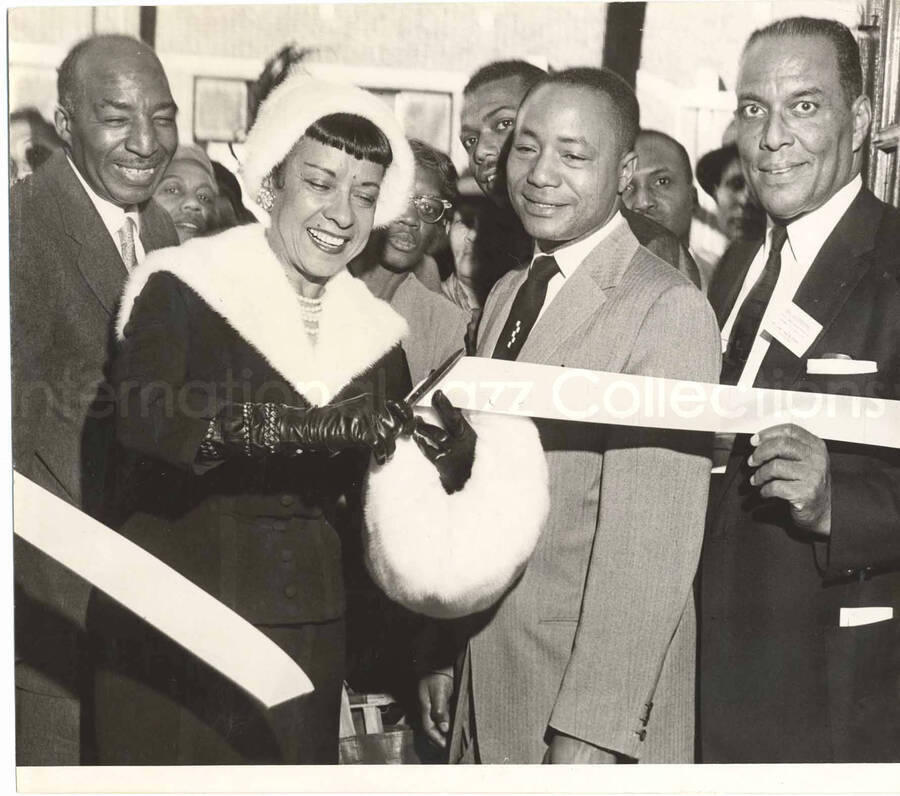 8 x 9 inch photograph. Gladys Hampton cuts a ribbon for an opening ceremony