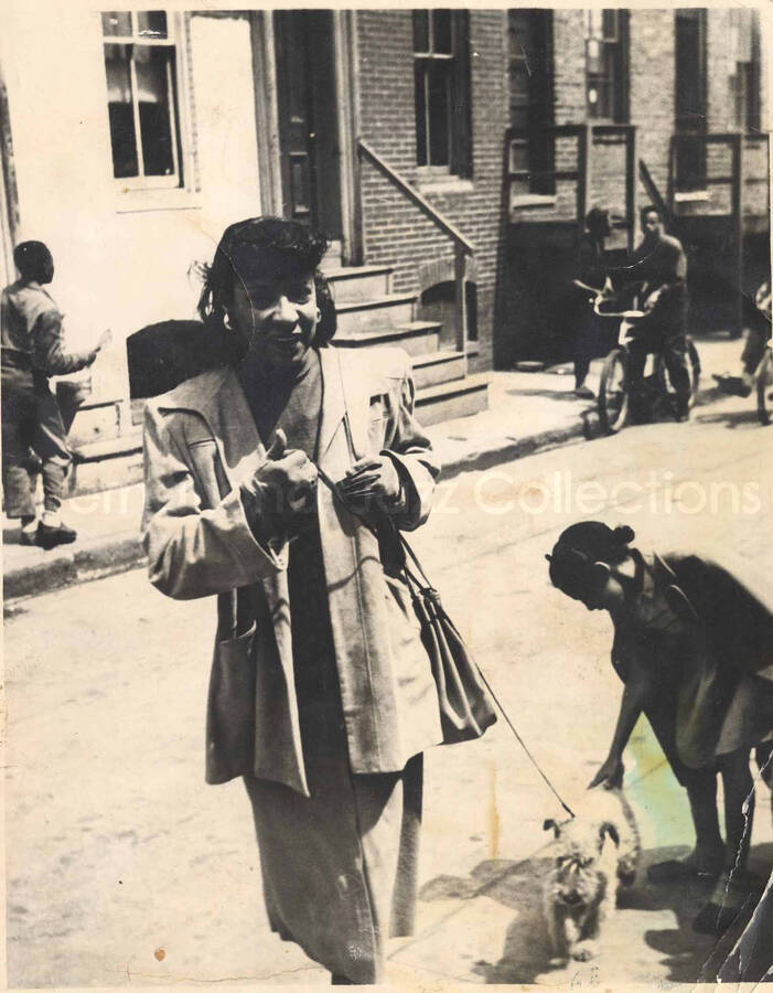 10 x 8 inch photograph. Gladys Hampton walking a white Scottie dog on a street with children playing around