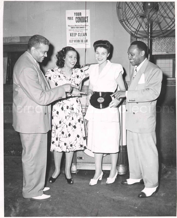10 x 8 inch photograph. Lionel and Gladys Hampton with unidentified man and woman in a club. The woman is holding the record Hamp Tone. There is a poster on the wall from the Citizens Committee of South Central District whose chairman was Clinton A. Brown