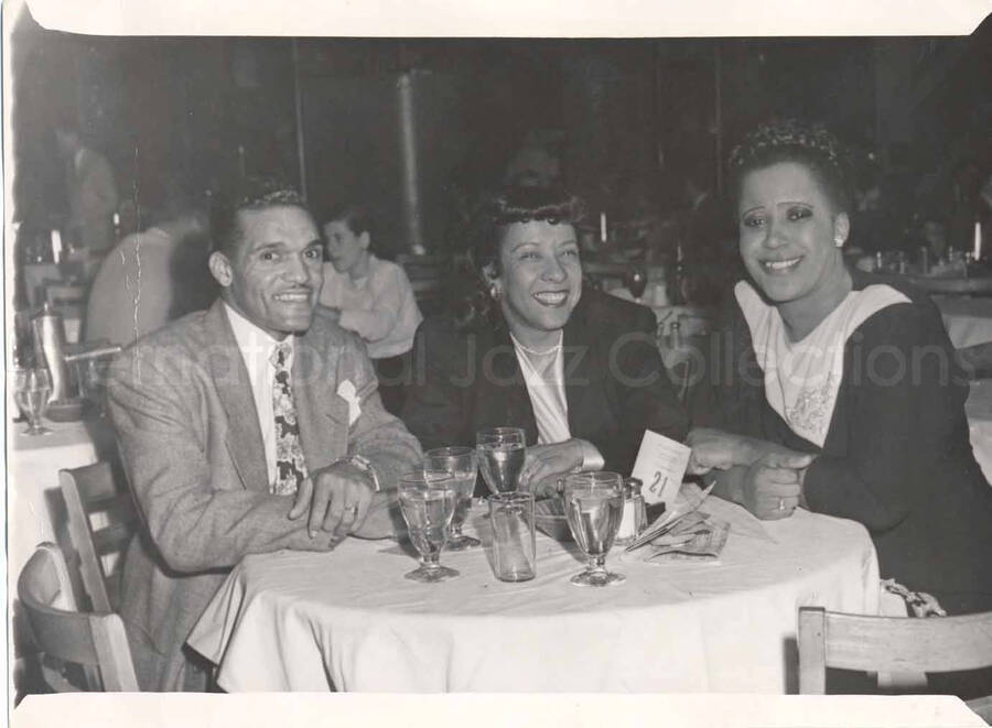 5 x 7 inch photograph. Gladys Hampton with unidentified man and woman in a restaurant