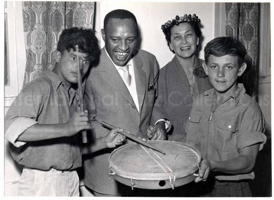 5 x 6 1/2 inch photograph. Lionel Hampton with unidentified woman visiting with children [at Swiss Village] in Israel