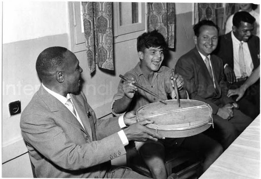 5 x 7 inch photograph. Lionel Hampton with unidentified man visiting with children [at Swiss Village] in Israel. Seen in the background is Leo Moore