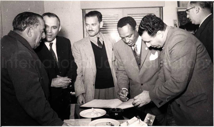 5 x 8 inch photograph. Gladys and Lionel Hampton with band in Israel. Lionel Hampton is signing a book with unidentified men