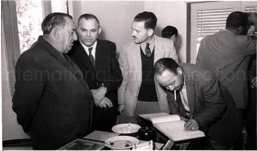 5 x 8 inch photograph. Gladys and Lionel Hampton with band in Israel. Billy Mackel signing a book with unidentified men