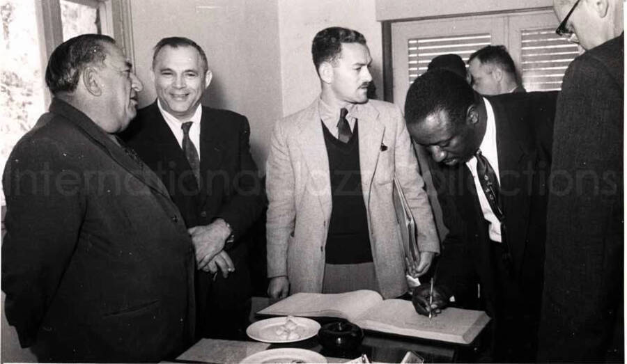 5 x 8 inch photograph. Gladys and Lionel Hampton with band in Israel. A member of the Lionel Hampton's band signing a book with unidentified men