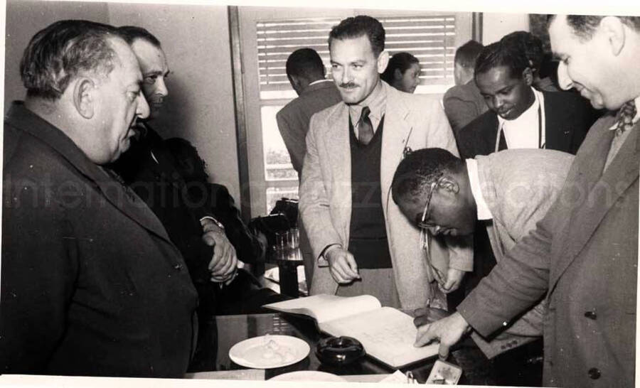 5 x 8 inch photograph. Gladys and Lionel Hampton with band in Israel. A member of the Lionel Hampton's band signing a book with unidentified men